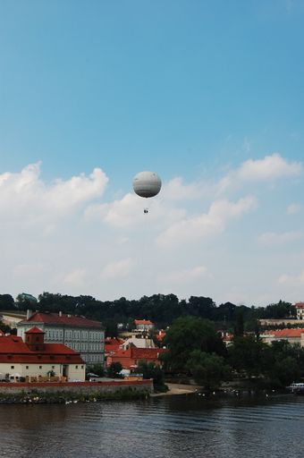 A vertical shot of the white hot air balloon flying over the riverside city with dense vegetation