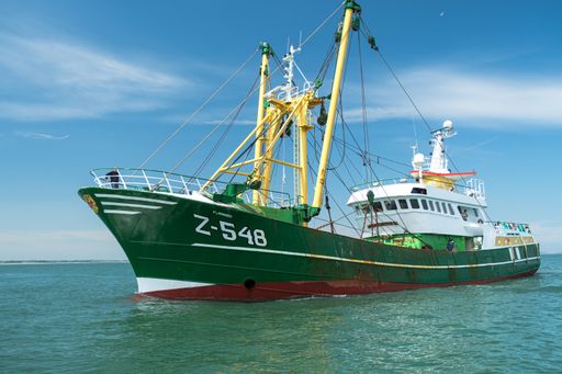 A green fishing vessel entering the Howth port marina on sunny day