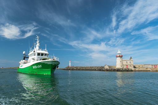 A green fishing vessel entering the Howth port marina on sunny day