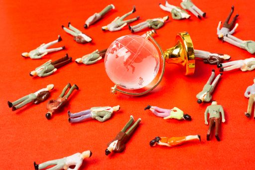 A closeup of a glass globe and human miniature figurines on a red background - concept of global quarantine during the COVID-19