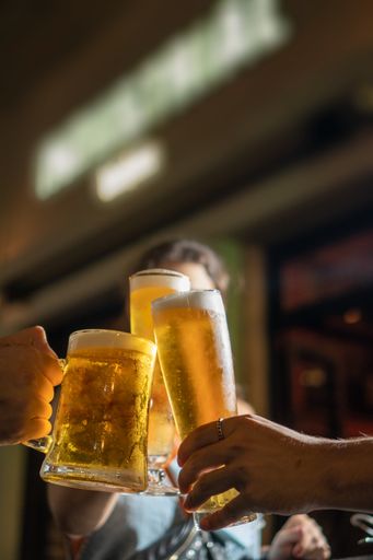A vertical shot of male hands clinking with glasses of refreshing cold beer in the bar