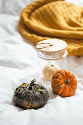 A vertical shot of small pumpkins near the orange blanket on the white sheet and in the jar