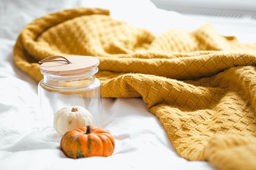 A vertical shot of small pumpkins near the orange blanket on the white sheet and in the jar