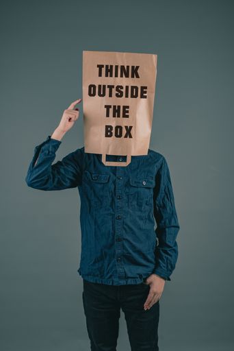 Young men has a paper bag on his head, the phrase think outside the box is standing on it, brainstorming for new ideas, be innovative