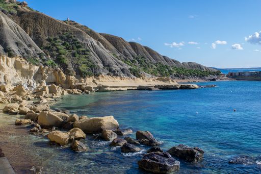 Steep blue clay slopes, with flaking debris forming scree on limestone along the coast of Xatt l-Ahmar, Ghajnsielem, Gozo, Malta, on a sunny day.