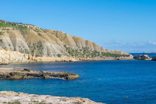 Steep blue clay slopes, with flaking debris forming scree on limestone along the coast of Xatt l-Ahmar, Ghajnsielem, Gozo, Malta, on a sunny day.