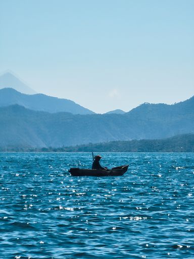 vertical shot of fisherman in large lake surrounded by mountains