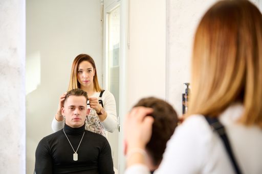 A closeup shot of a man in a hairdresser salon and the barber hairdressing the hair with her hands