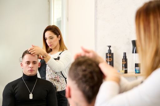 A closeup shot of a man in a hairdresser salon and the barber hairdressing the hair with her hands