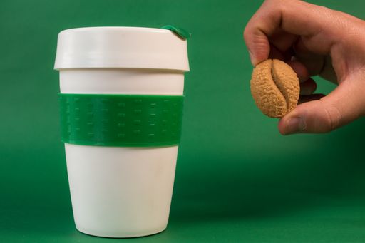 A white thermos and a hand holding a coffee bean on a green background