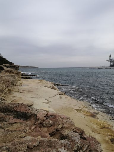 A vertical shot of rocky seashore under cloudy sky