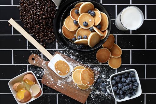 A top view of a messy black tiled kitchen table with ingredients for cooking blueberry pancakes