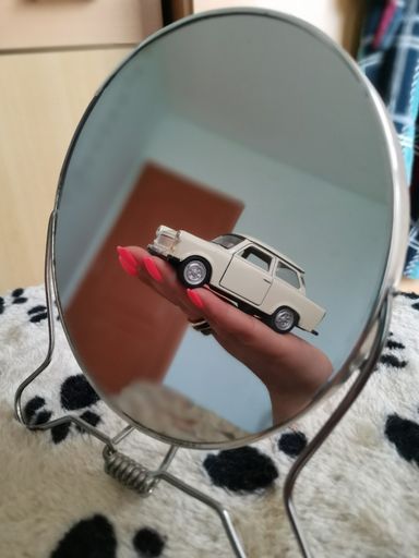 A vertical closeup shot of a mirror reflecting a small white toy car in a female's hand