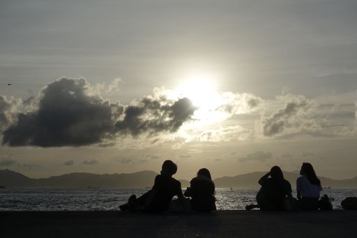 A back view of people sitting near the sea during sunset in Hong Kong, China