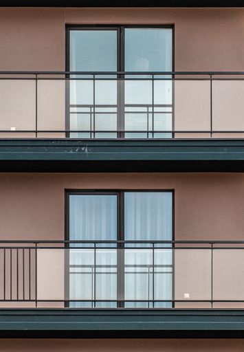 A vertical symmetric shot of two balconies and windows with pink walls and modern design