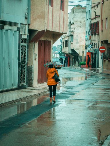 A female with a yellow jacket and umbrella walking in empty street on a rainy day