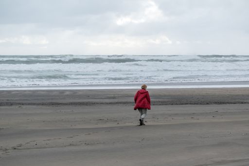 A landscape shot of a  female in red coat walking towards the ocean