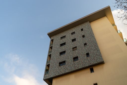 A low angle shot of beige and black building facade with the last floors under blue bright sky