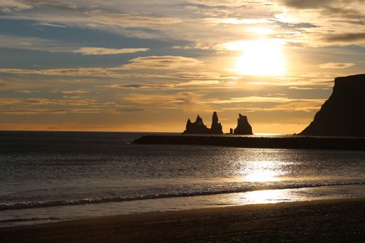 A beautiful scene of a beach near shiny water near rocky cliffs against a sunny golden sunset sky