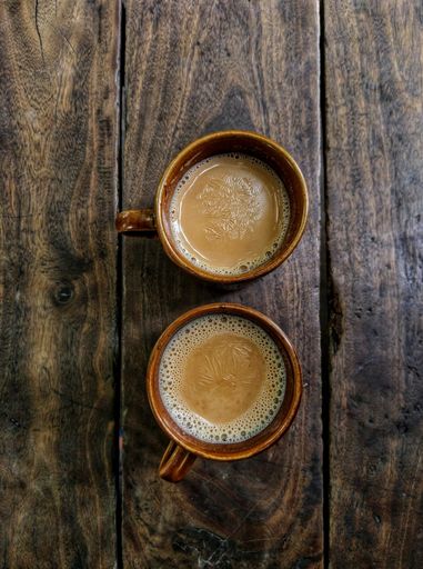 A top view of two cups of coffee in brown mugs on a wooden table