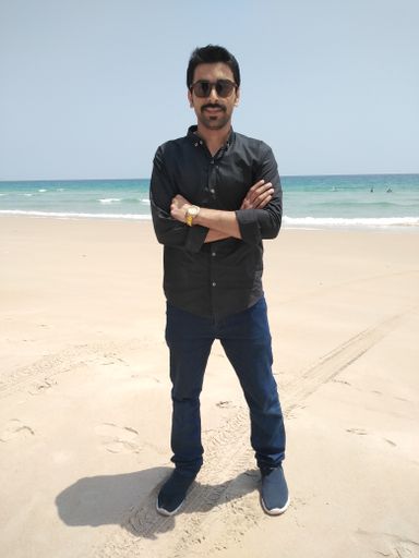 A vertical shot of man in black shirt and sunglasses on a sandy beach