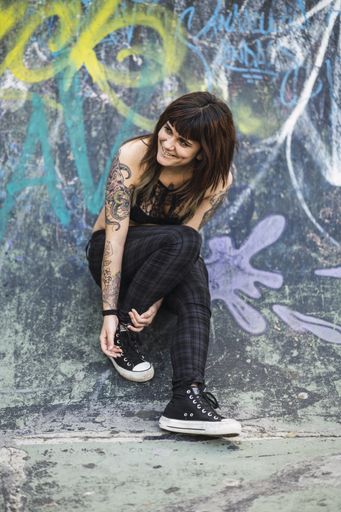 A young attractive Caucasian female with tattoos standing against a skating ramp