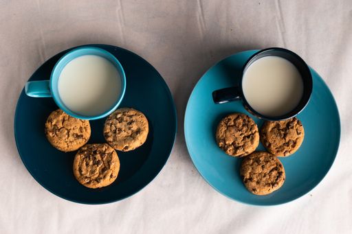 A top view of two blue mugs of milk and chocolate chip cookies around it