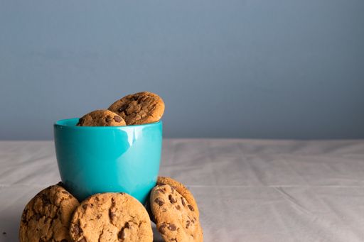 A selective focus shot of a blue mug of milk and chocolate chip cookies around it