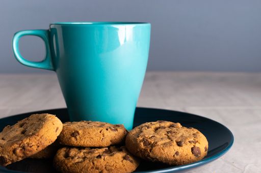 A selective focus shot of a blue mug of milk and chocolate chip cookies around it