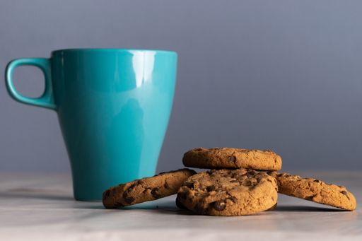A selective focus shot of a blue mug of milk and chocolate chip cookies around it