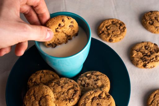 A selective focus shot of a person dipping chocolate chip cookies in a cup of milk