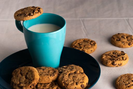 A selective focus shot of a blue cup of milk and chocolate chip cookies