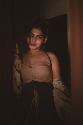 A vertical shot of an Indian female posing in the dark and wearing beige top and black pants