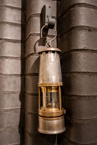 A vertical shot of an old oil lamp hanging from the hanger on the brown wall