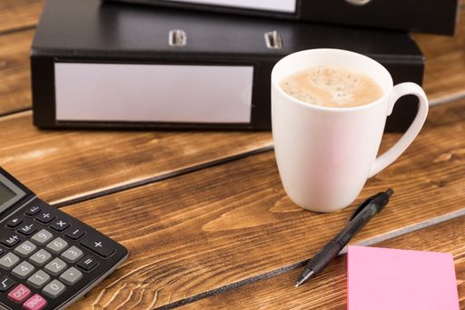 A closeup shot of a desk with coffee cup, folder, calculator and pen