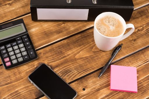A closeup shot of a desk with coffee cup, folder, calculator and pen