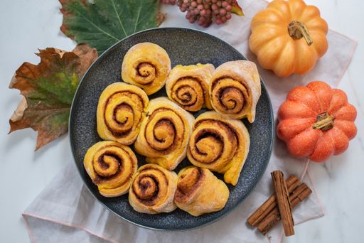 A top view of cinnamon rolls on a black plate with cinnamon sticks and pumpkins next to