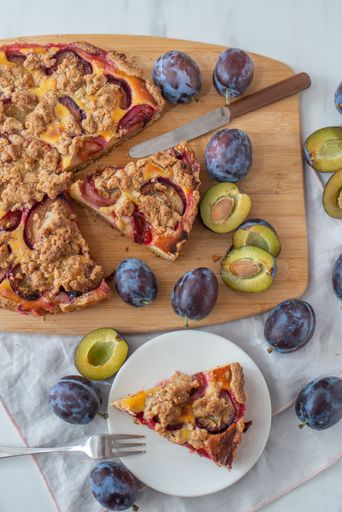 A top view of a sliced homemade plum crumble pie on a table