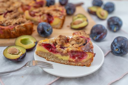 A closeup shot of a slice of homemade plum crumble pie on a white plate
