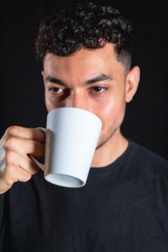 A vertical closeup of the man drinking from a white mug isolated on black background.