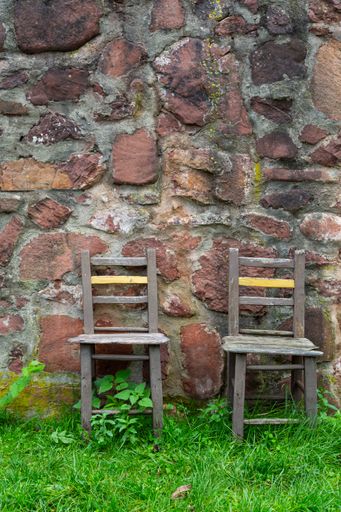 A vertical shot of empty wooden chairs against an old stone wall