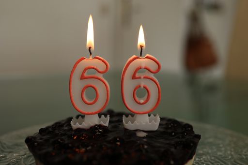 A closeup of a birthday cake with burning candle number 66