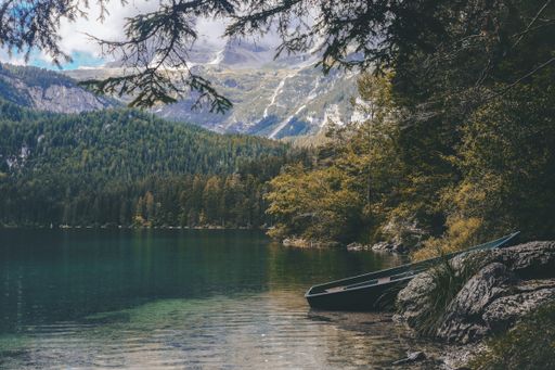 A beautiful shot of a boat near the lake surrounded by green trees and high mountains during daylight
