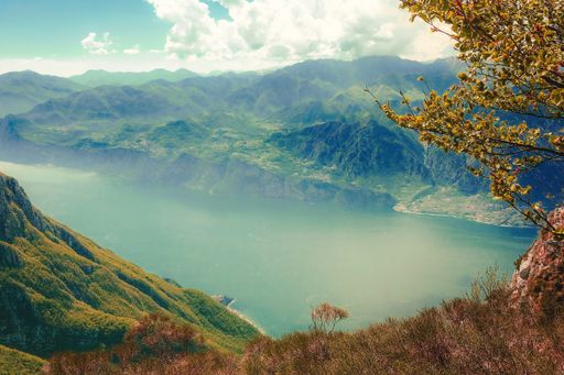 A high angle shot of a lake surrounded by green mountains covered in fog under the cloudy sky