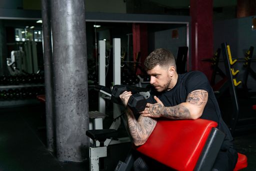 Tattooed man doing exercise with hand weigths in the gym. Healthy lifestyle, workout concept, copy space