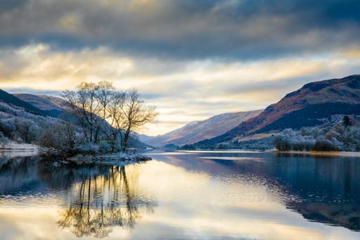 A landscape view of a lake surrounded by mountains under a cloudy sky