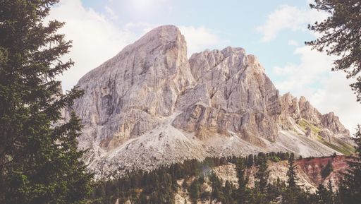 A beautiful shot of high rocky mountains surrounded by green trees under the cloudy sky in San Martino, Badia