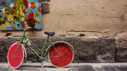 A wide shot of a unique watermelon bicycle leaning on an old wall during daytime