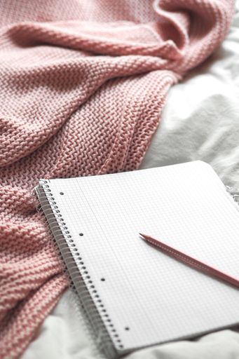 A closeup of a notebook with a pencil on a white and pink fabric