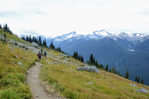 A landscape shot of two persons walking on hiking road with snowy mountains in the back